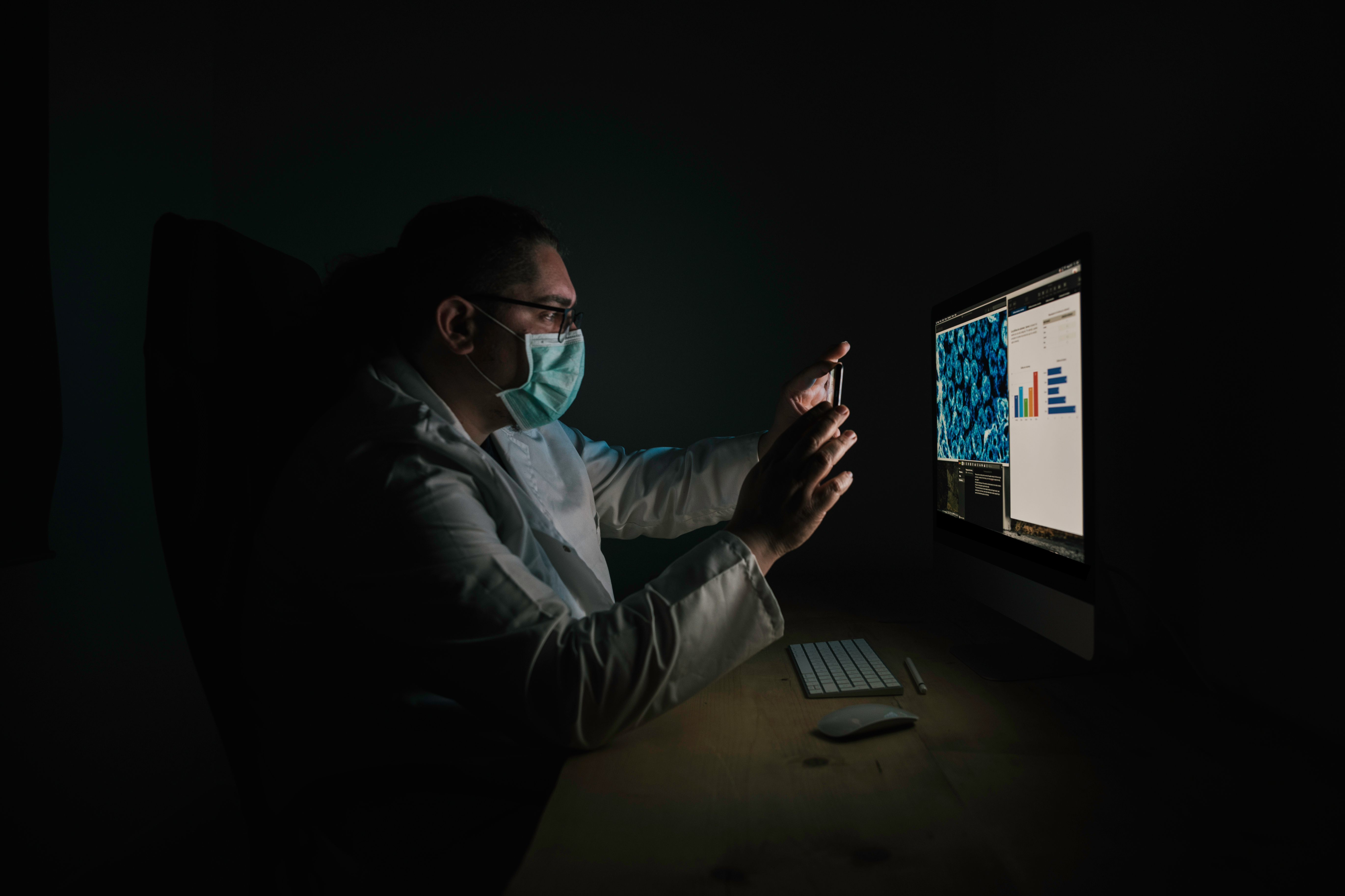 Stock photo of doctor taking screen shot with medical results. He wears a white coat and a protective mask.