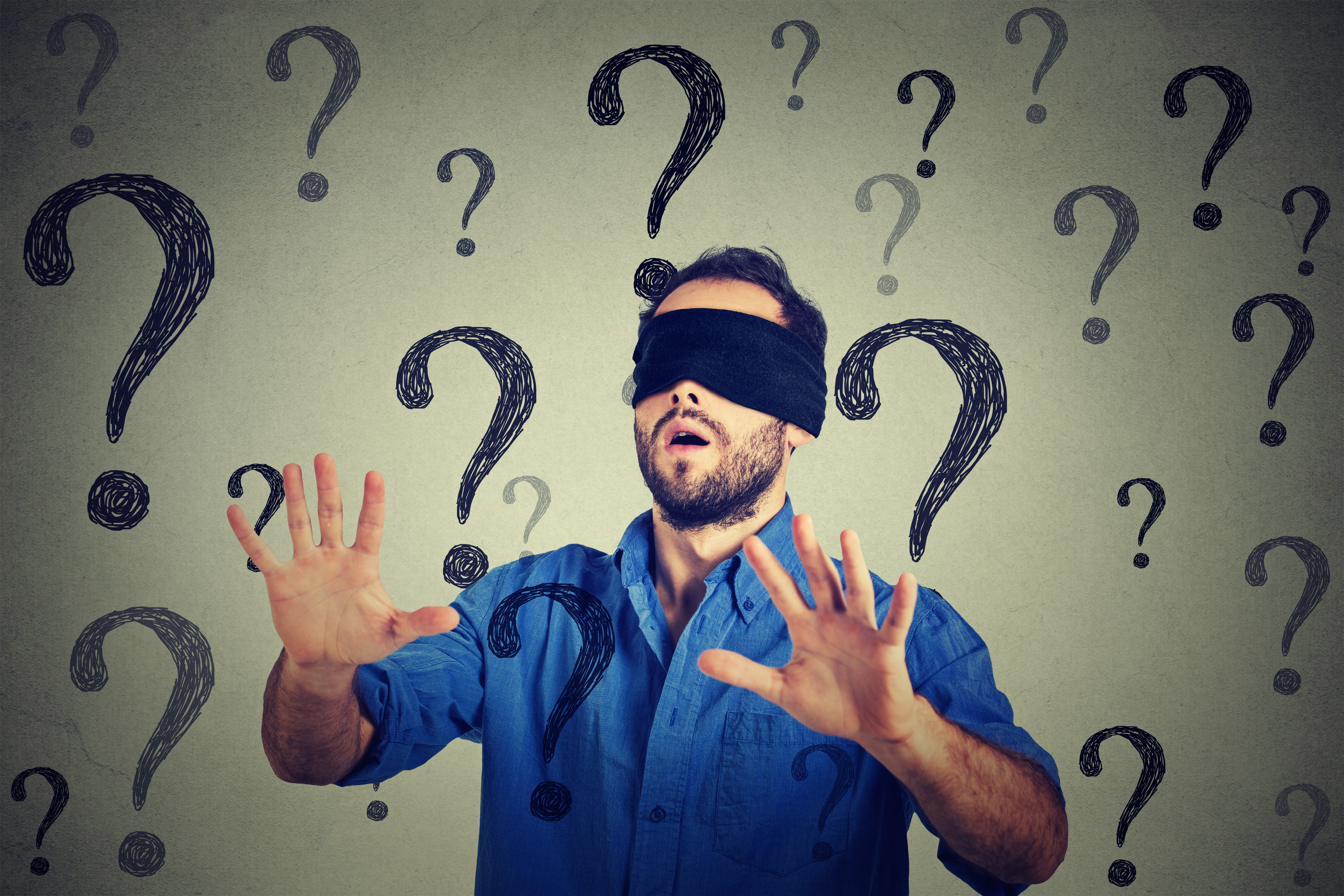 Portrait business man blindfolded stretching his arms out walking through many questions isolated on gray wall background