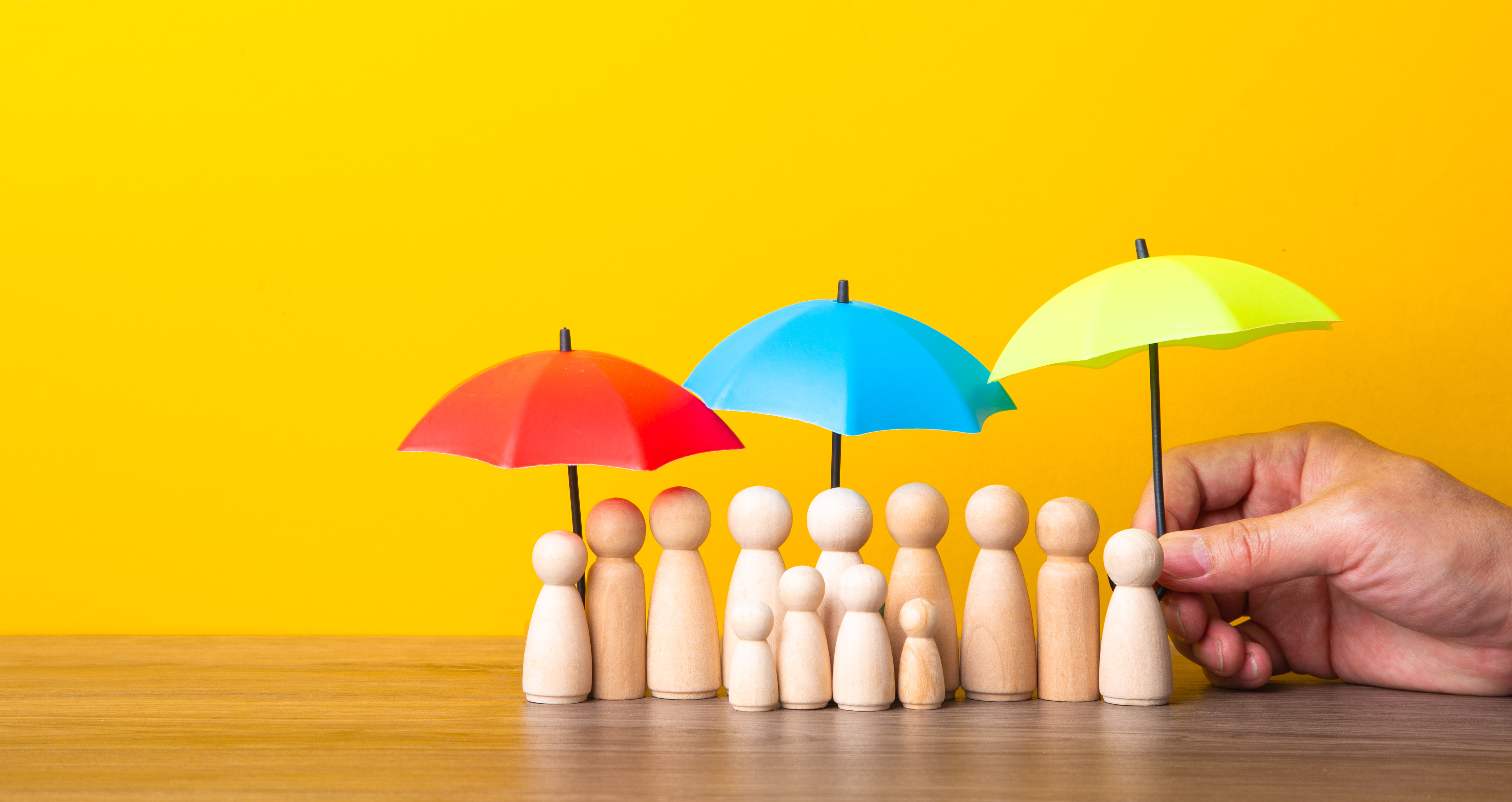 People protection, insurance and safety concept. Many wooden people figures under umbrella on yellow background.
