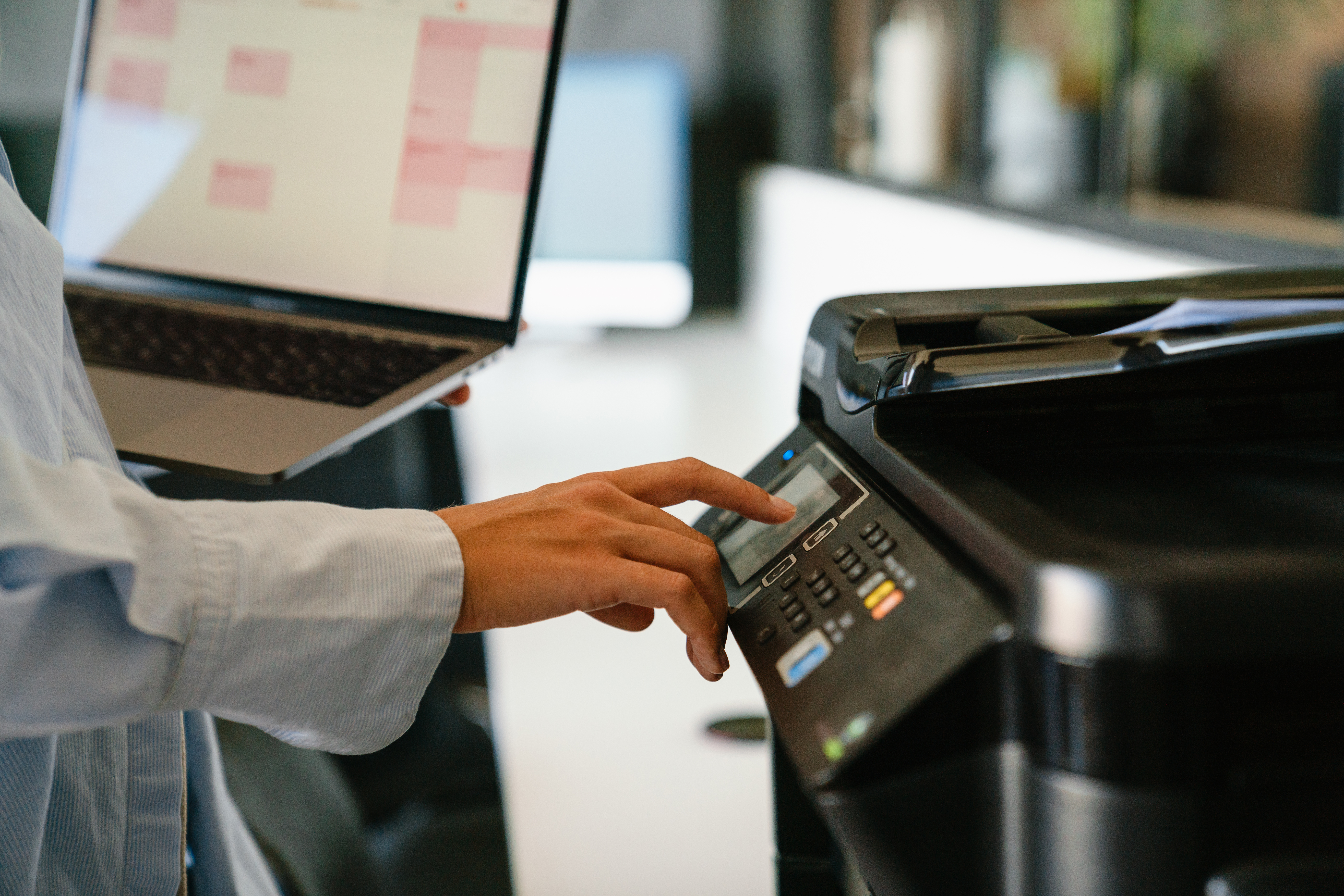 Close up of business woman holding laptop and using printer while standing in modern office